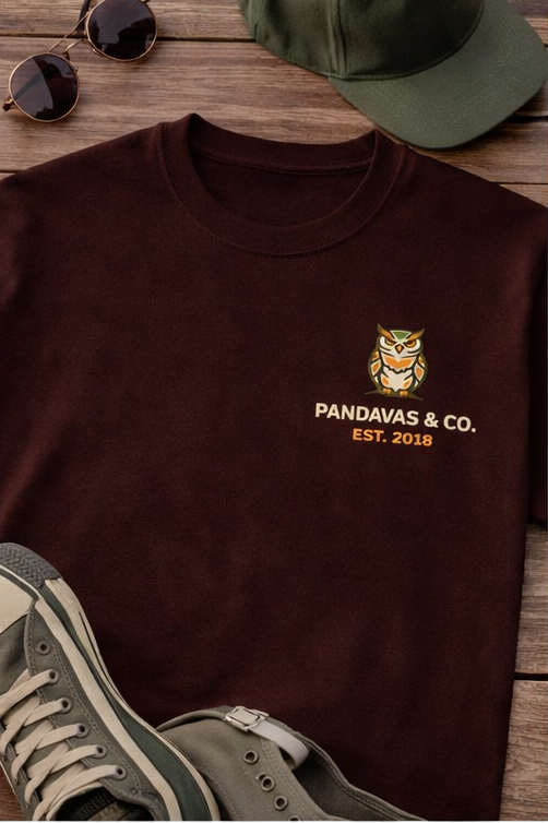Brown t-shirt with 'Pandavas & Co.' logo and text, paired with a green cap and sunglasses on a wooden surface.